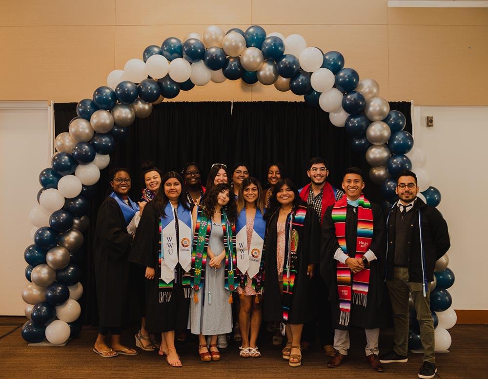 A group of students in graduation gowns under a balloon arch